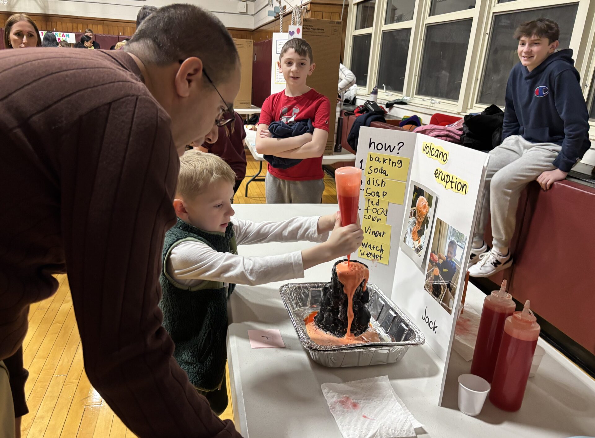IMG_3168 South Row Elementary School Assistant Principal Dr. Jayson Ramalho watches as first grader Jack Doubrava makes his volcano erupt during the school's science fair.